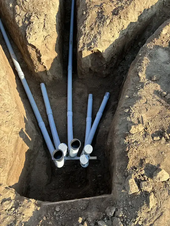Grey electrical conduits sweeping up out of an open utility trench to capped stub-ups in the dirt.