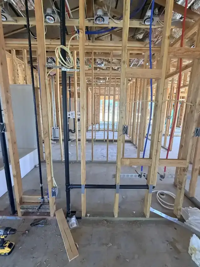 Rough-in wiring and recessed light cans run through the wood framing of a house under construction.