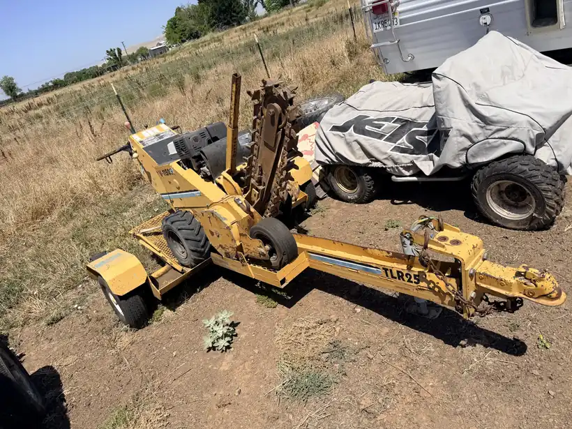 Yellow trencher with its chain digging boom raised, hitched to a tow bar on a dry lot.
